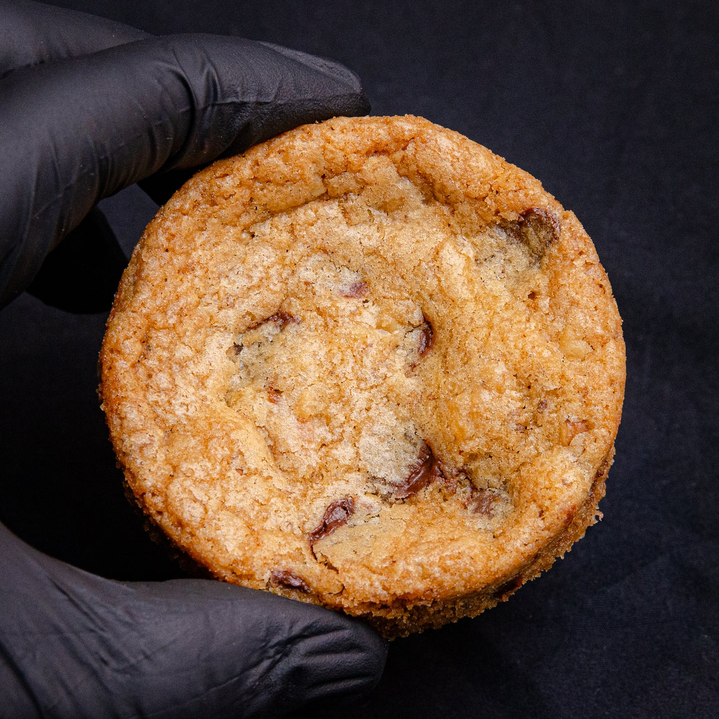A single chewy walnut chocolate chip cookie held in a person's hand, with the cookie showing chunks of walnut and chocolate throughout the dough.